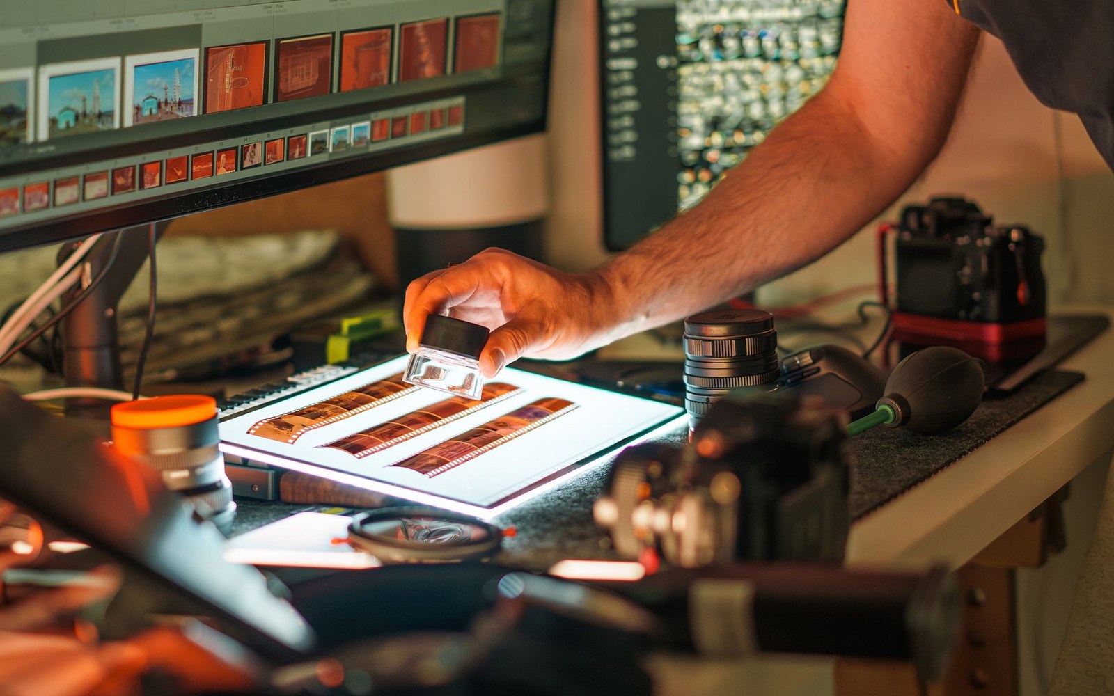 An editor's hand over a lightbox, film strips and a loupe on the bench