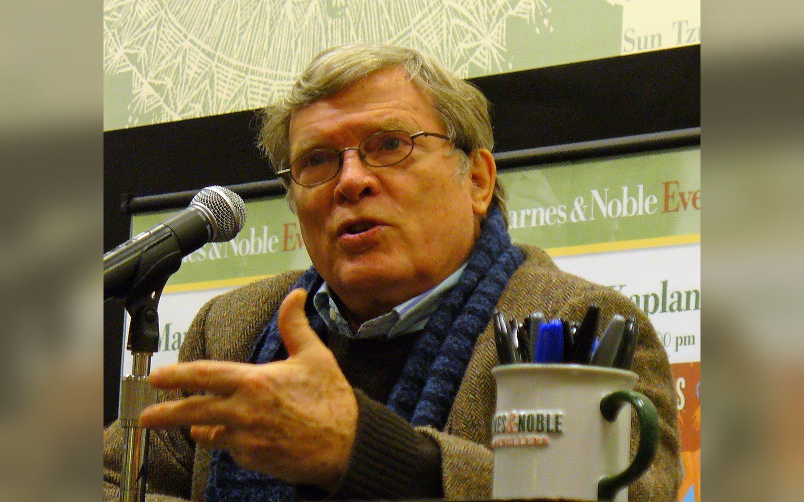 Man in glasses and scarf speaks at a microphone during a Barnes & Noble event