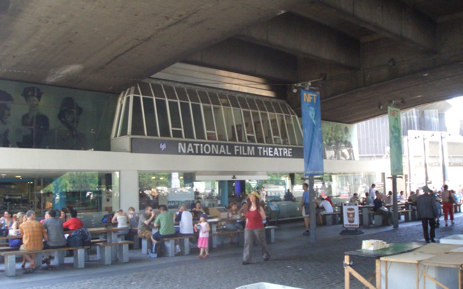 People sit at outdoor tables beneath the National Film Theatre entrance under a concrete overpass