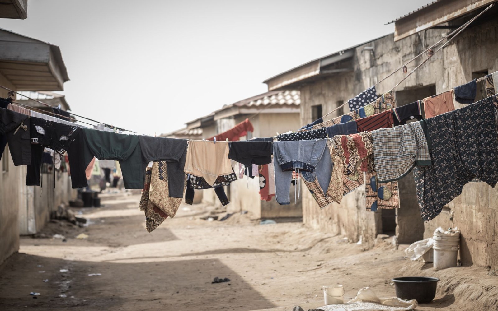 Clothes hang on lines strung between buildings in a narrow dirt alley