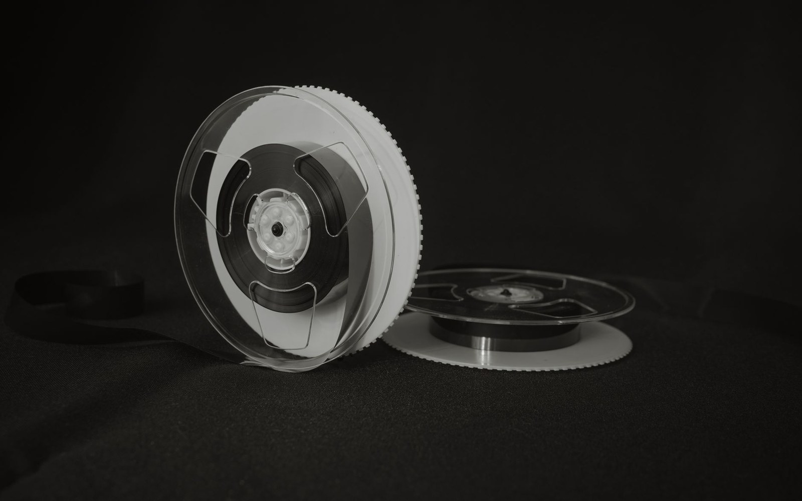 Two reel-to-reel film tape reels resting against a dark background