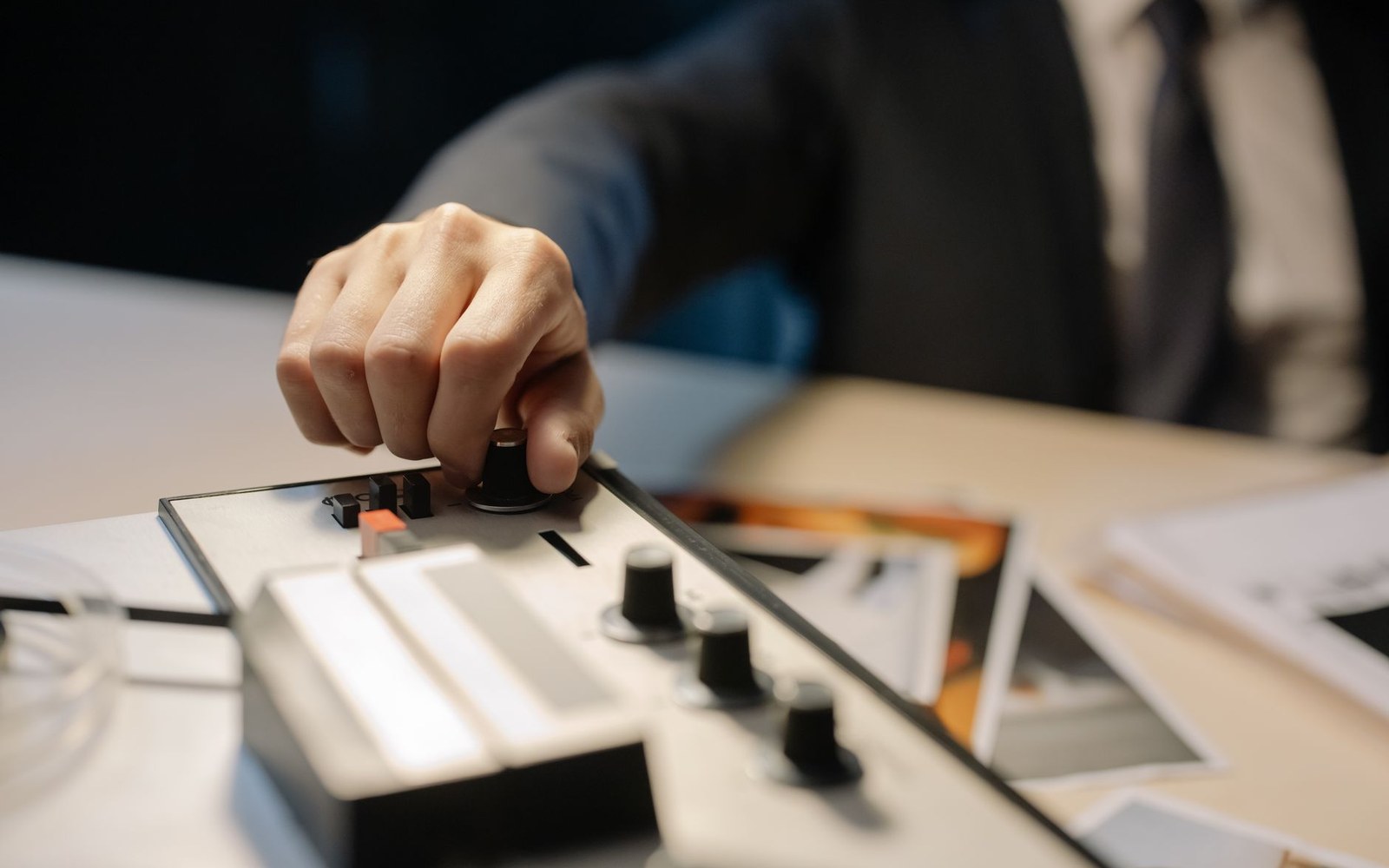 A hand on the transport controls of a reel-to-reel tape recorder, photographic material spread beside it